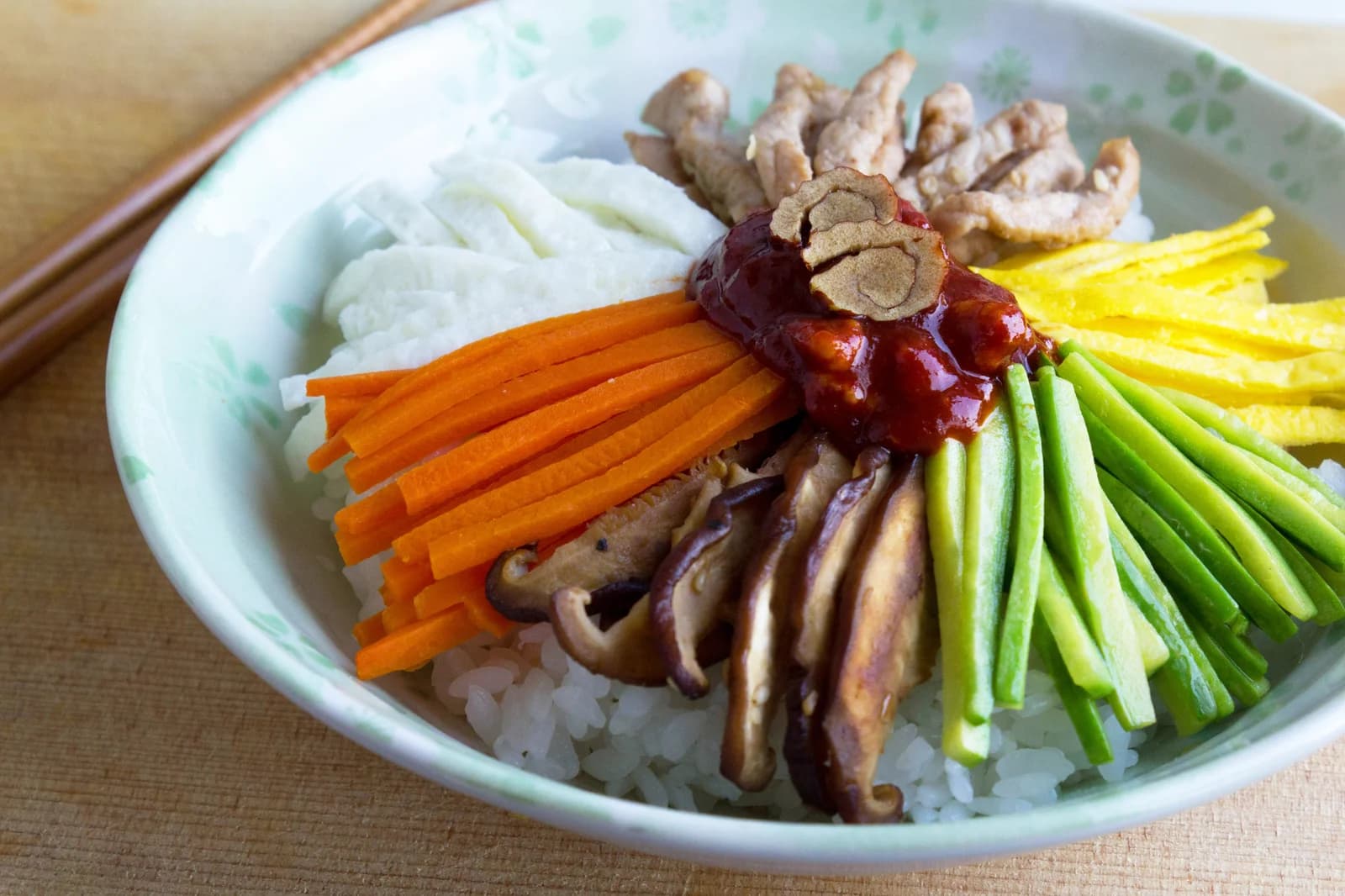 An unmixed bibimbap bowl with rice, colorful vegetables and red sauce in separate sections