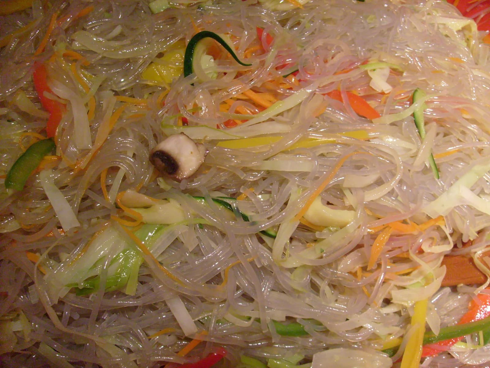 Close view of translucent japchae noodles mixed with sliced vegetables