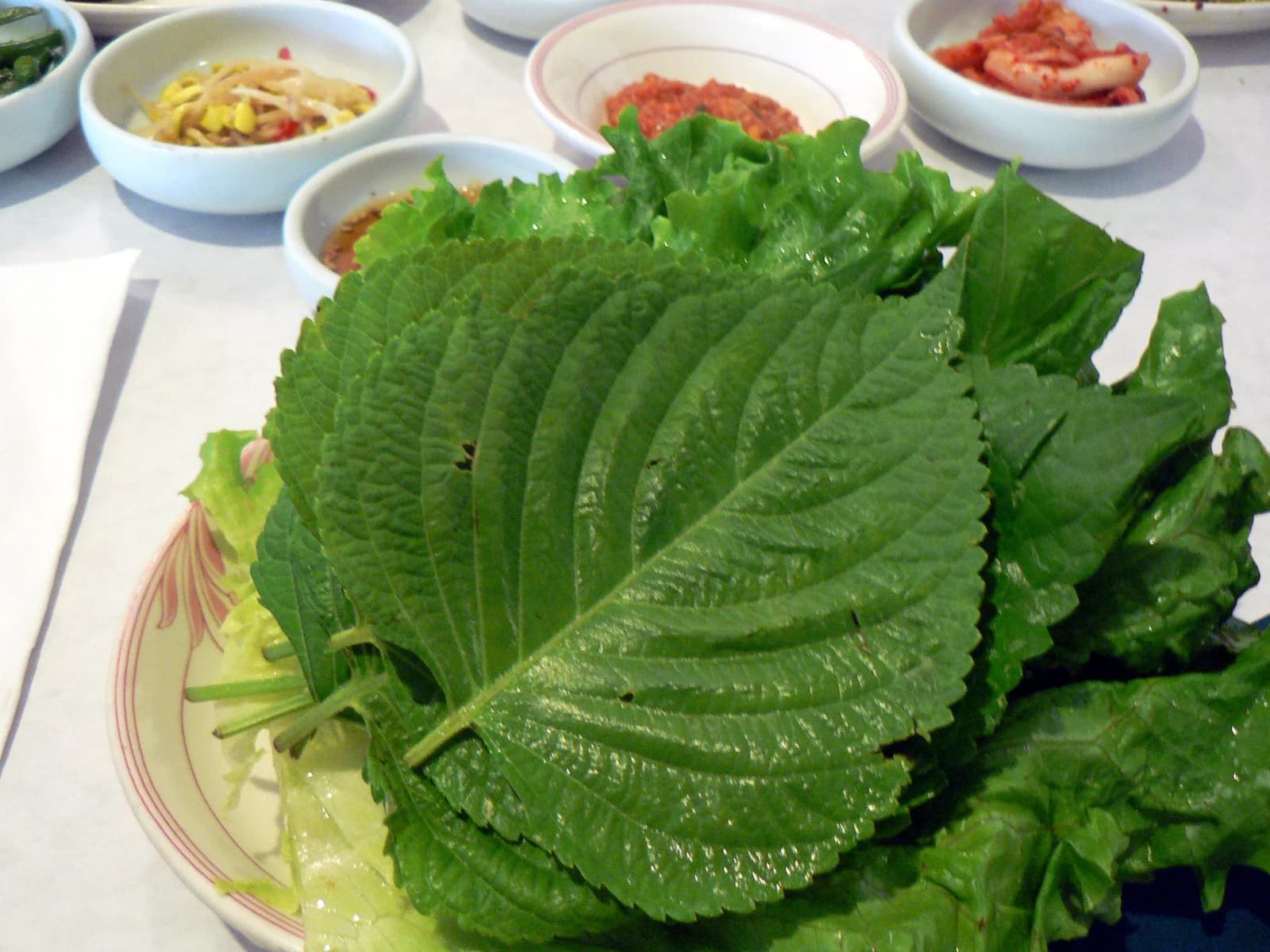 Perilla and lettuce leaves arranged on a plate with Korean side dishes behind them