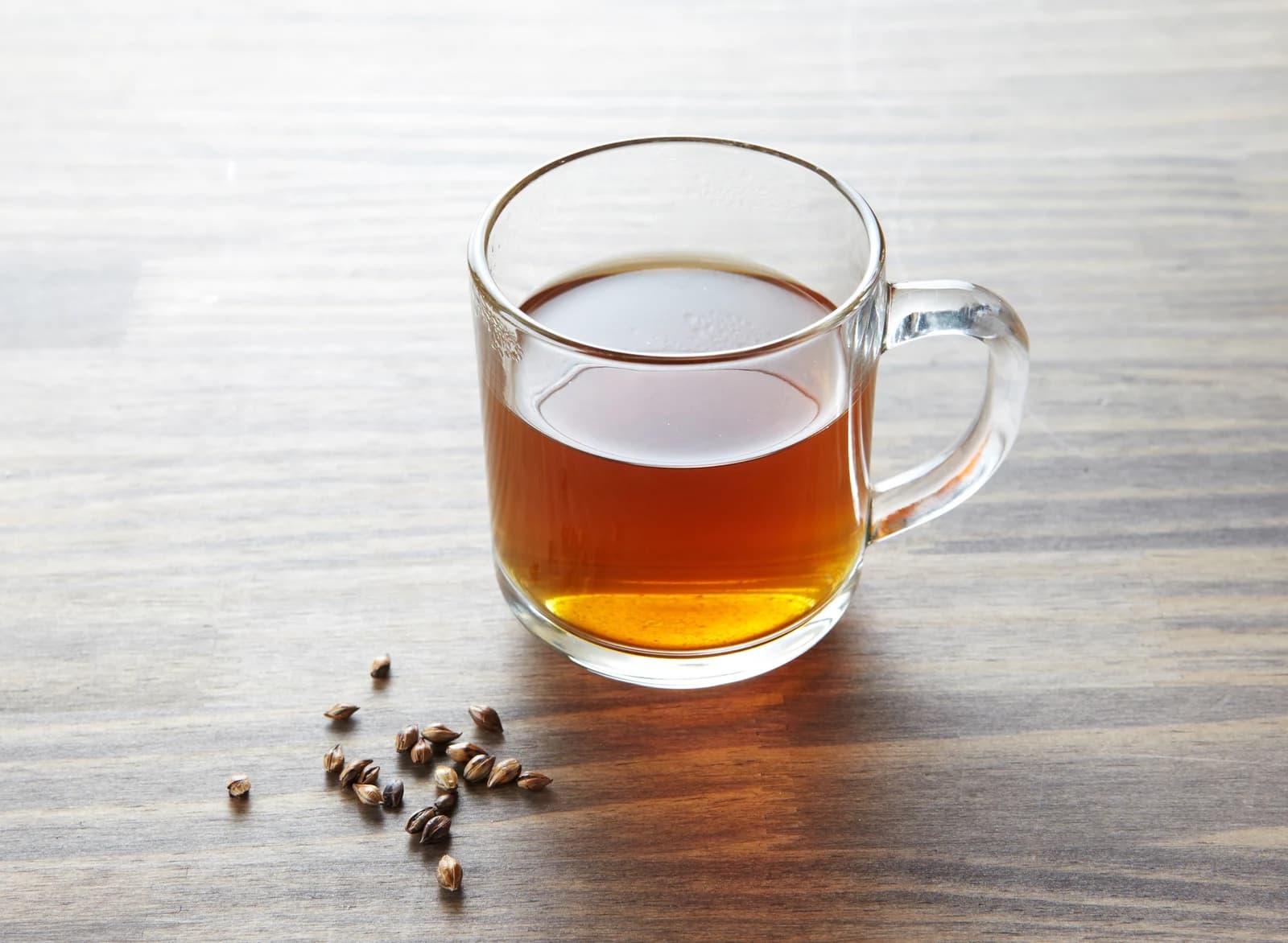 Amber boricha in a glass mug with roasted barley grains beside it.