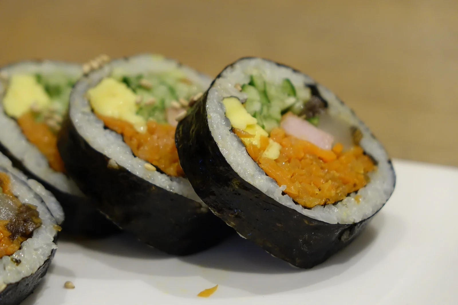 Slices of gimbap showing white rice, carrot and other fillings inside a dark seaweed wrapper