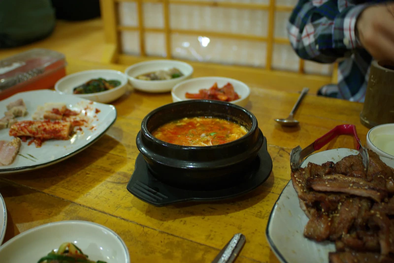 Dark earthenware ttukbaegi holding sundubu-jjigae on a trivet among dishes at a table in 2008