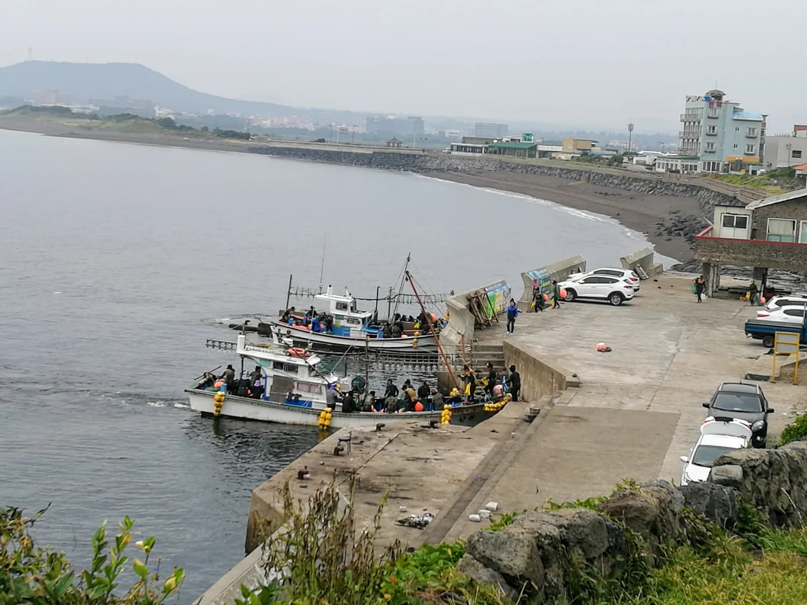 Haenyeo with diving equipment and orange floats beside fishing boats at a Jeju quay in 2017