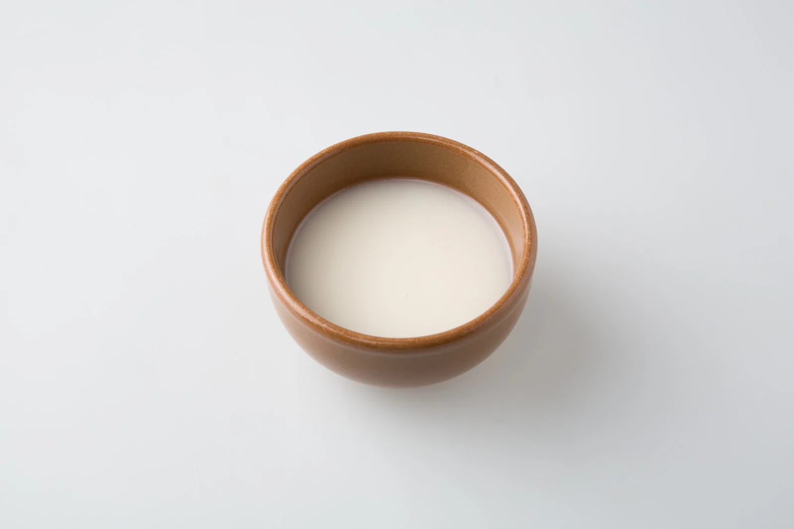 Cloudy pale makgeolli in a brown cup against a light background.