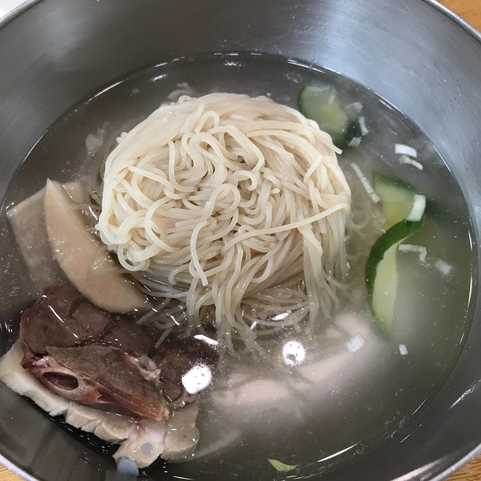 Mul-naengmyeon noodles in clear broth with cucumber and sliced meat.